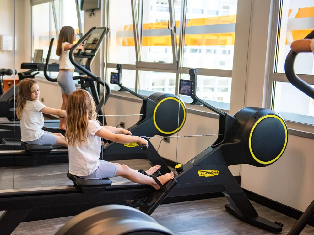 Bibione Palace Hotel · La tua casa al mare a 4 stelle S Bambina che usa un vogatore in palestra con grandi finestre