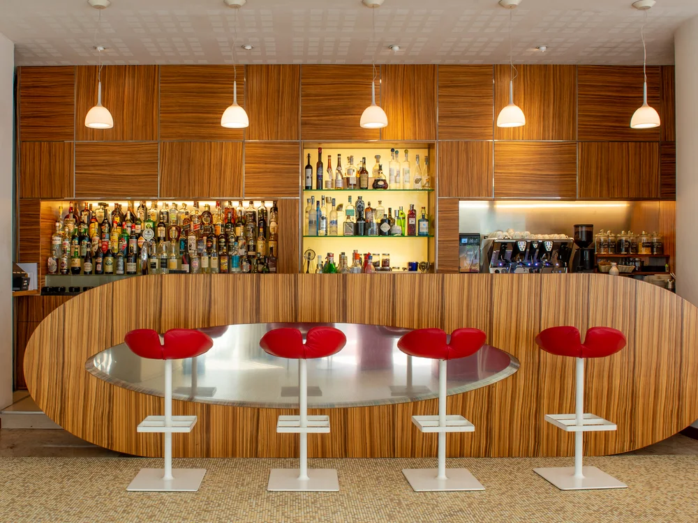 Bibione Palace Hotel · La tua casa al mare a 4 stelle S Bar moderno con sgabelli rossi e scaffali di bottiglie di alcolici