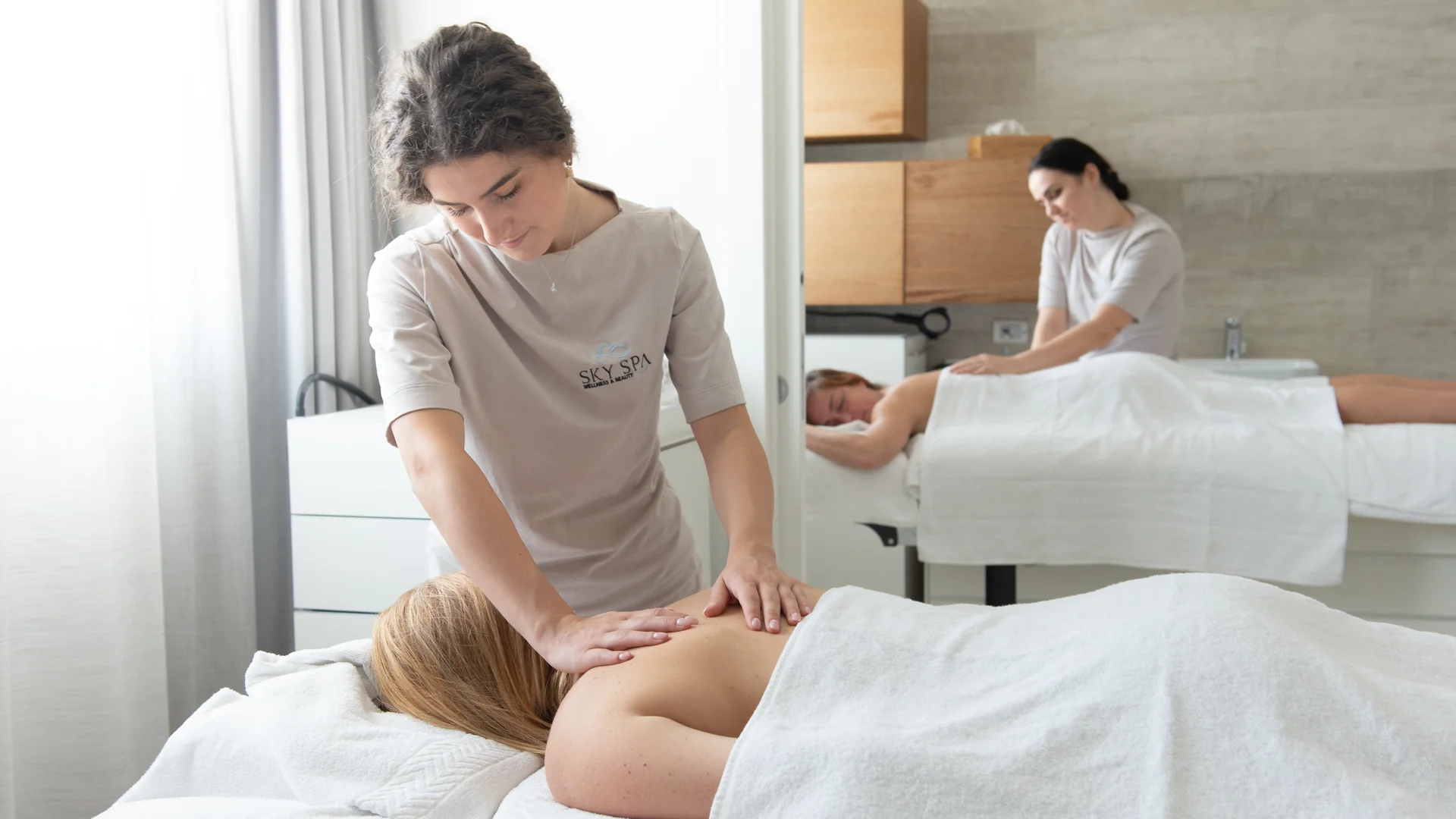 Massaggiatrici che fanno massaggi rilassanti a due clienti in una spa luminosa