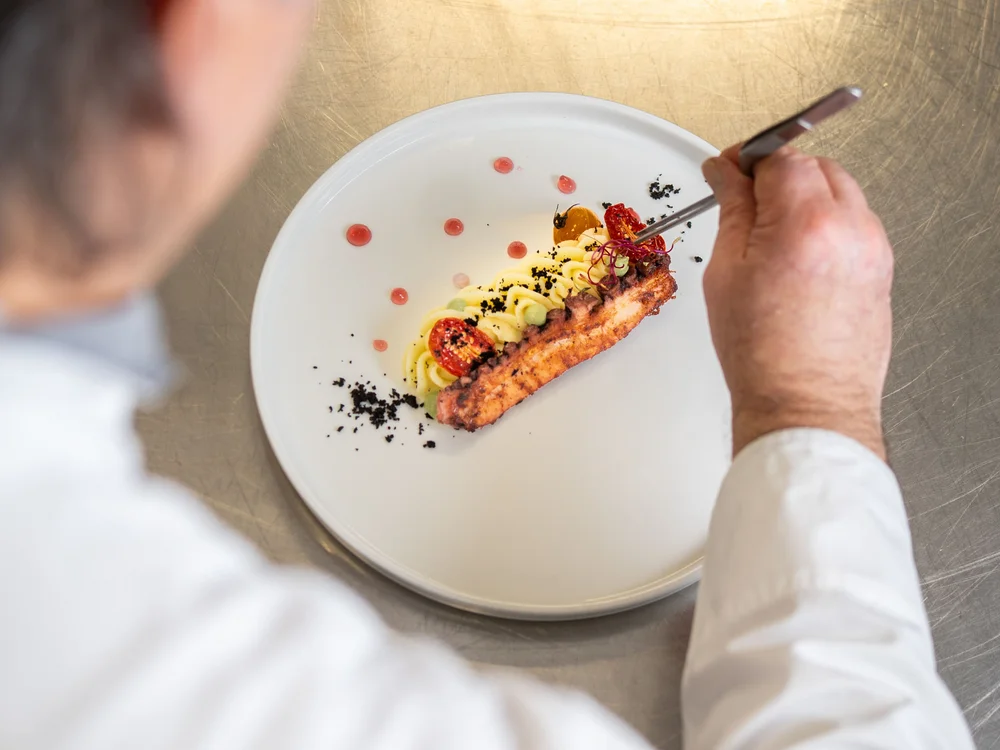 Bibione Palace Hotel · La tua casa al mare a 4 stelle S Chef che decora un piatto gourmet con pinzette in cucina