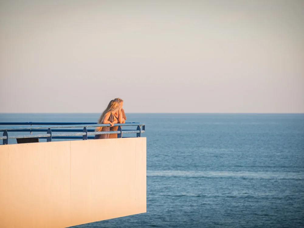 Bibione Palace Hotel · La tua casa al mare a 4 stelle S Due donne che guardano il mare da una terrazza con ringhiera blu