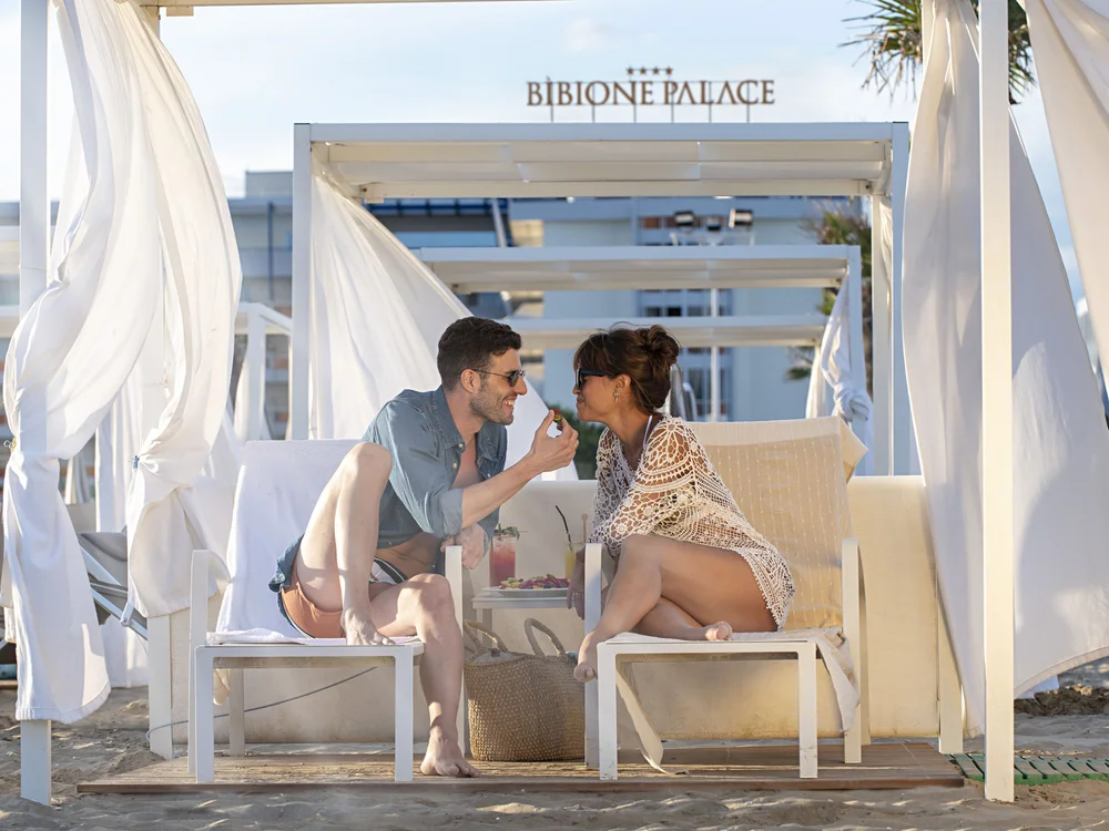 Bibione Palace Hotel · La tua casa al mare a 4 stelle S Coppia seduta sotto un gazebo bianco sulla spiaggia di Bibione Palace