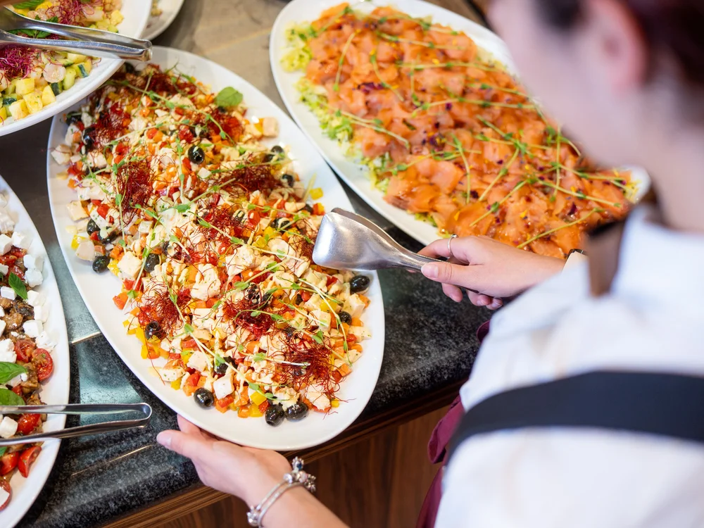 Bibione Palace Hotel · La tua casa al mare a 4 stelle S Persona che serve un piatto di insalata mista colorata al buffet