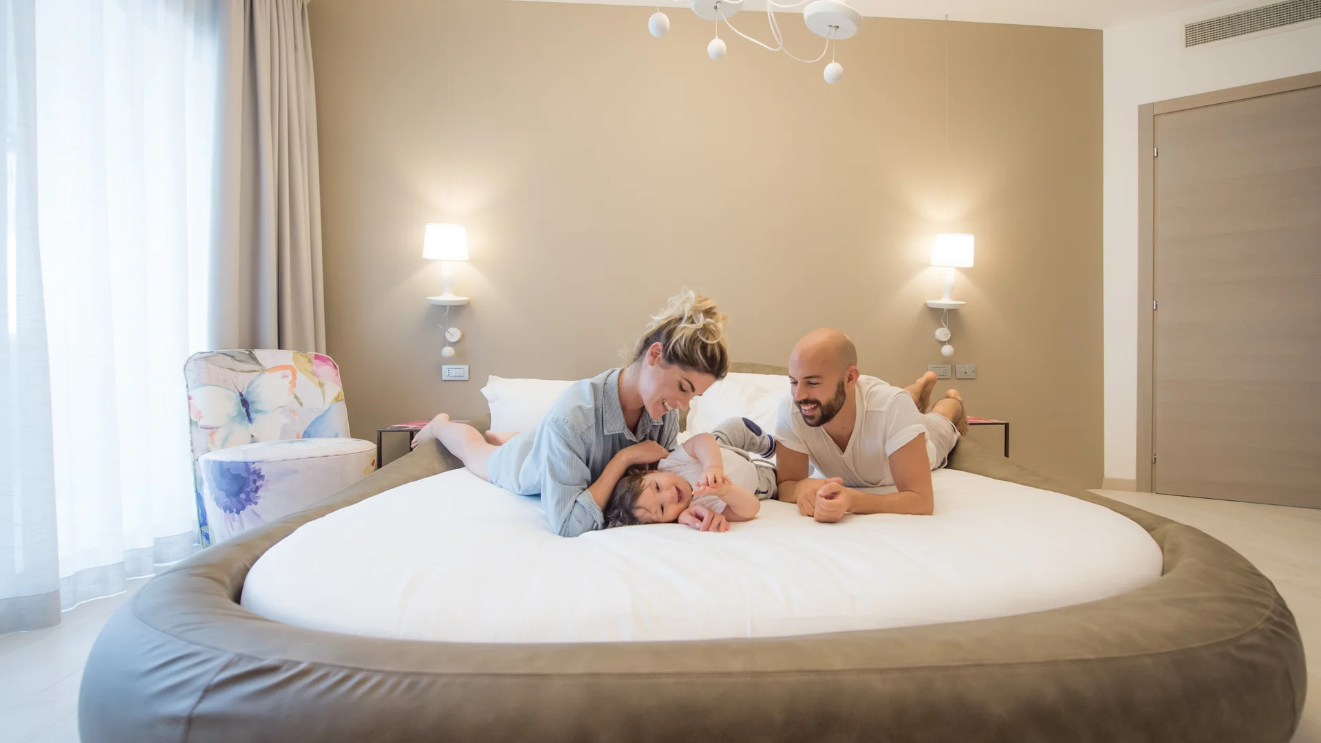 Famiglia felice sdraiata su un grande letto rotondo in una stanza luminosa