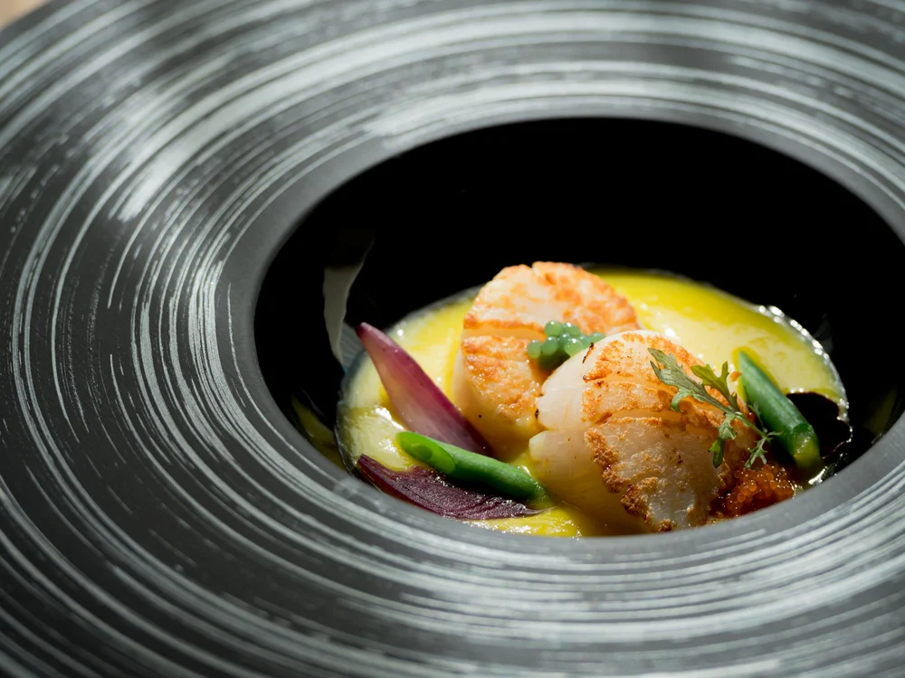 Bibione Palace Hotel · La tua casa al mare a 4 stelle S Capesante grigliate con verdure e salsa in piatto nero elegante