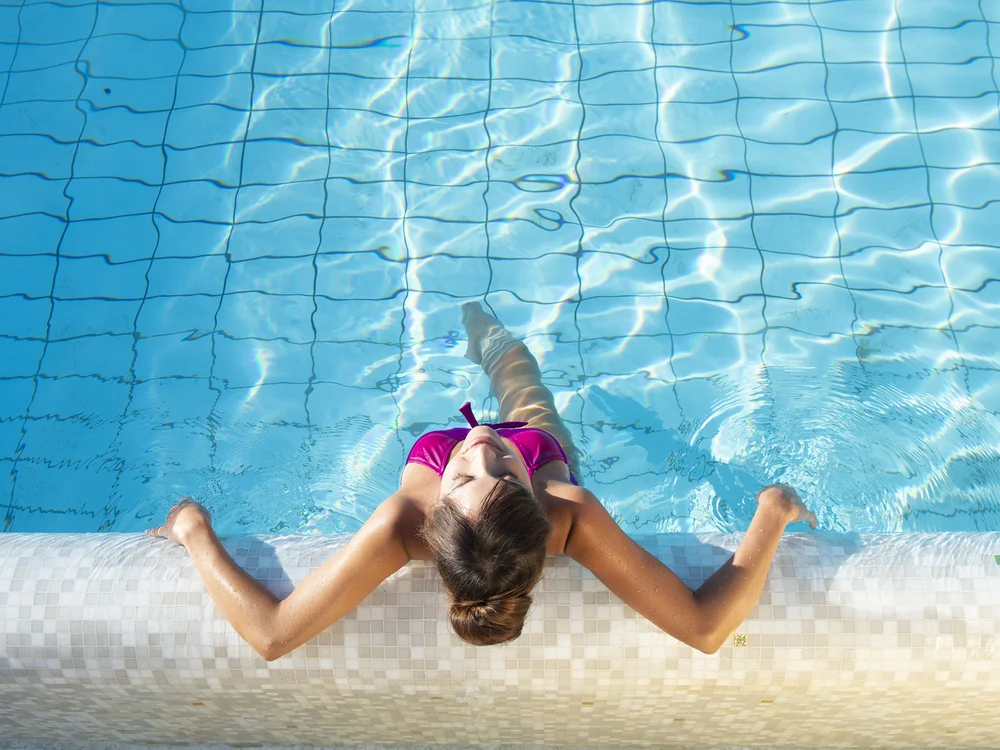 Bibione Palace Hotel · La tua casa al mare a 4 stelle S Donna in costume da bagno rosa che si rilassa in piscina appoggiata al bordo
