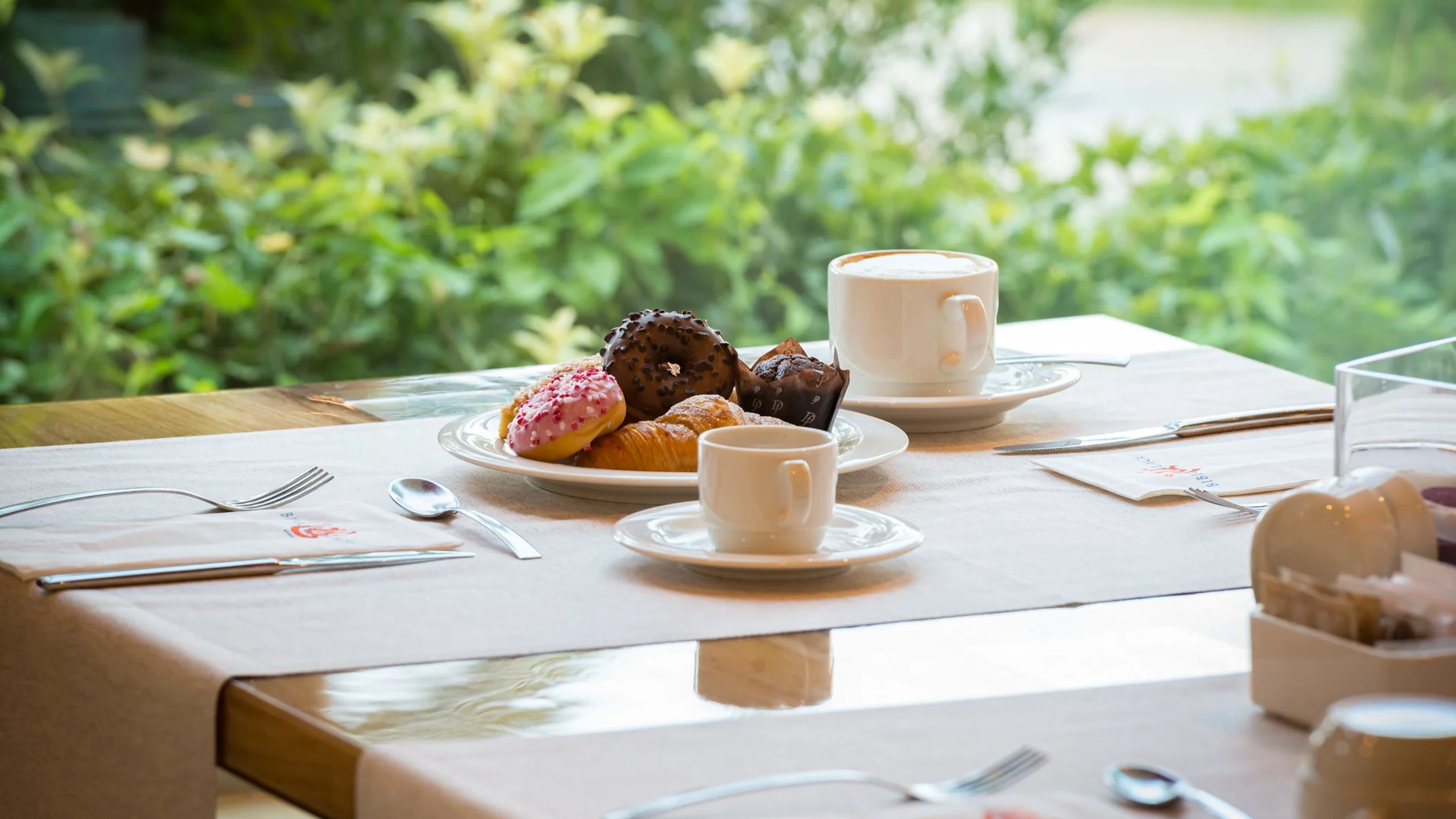 Colazione con caffè e dolci su un tavolo apparecchiato vicino a una finestra verde