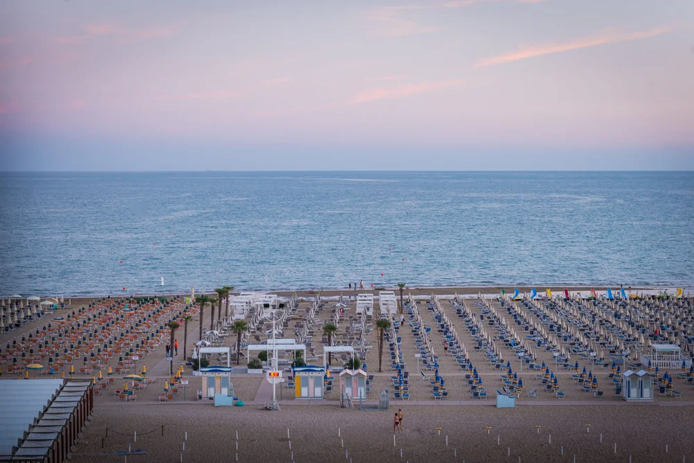 Spiaggia con file ordinate di ombrelloni e lettini di fronte al mare al tramonto
