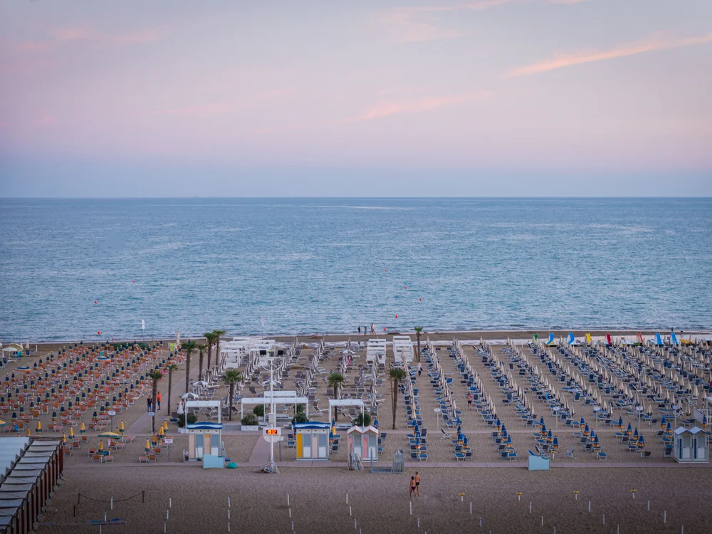 Bibione Palace Hotel · La tua casa al mare a 4 stelle S Spiaggia con file ordinate di ombrelloni e lettini di fronte al mare al tramonto