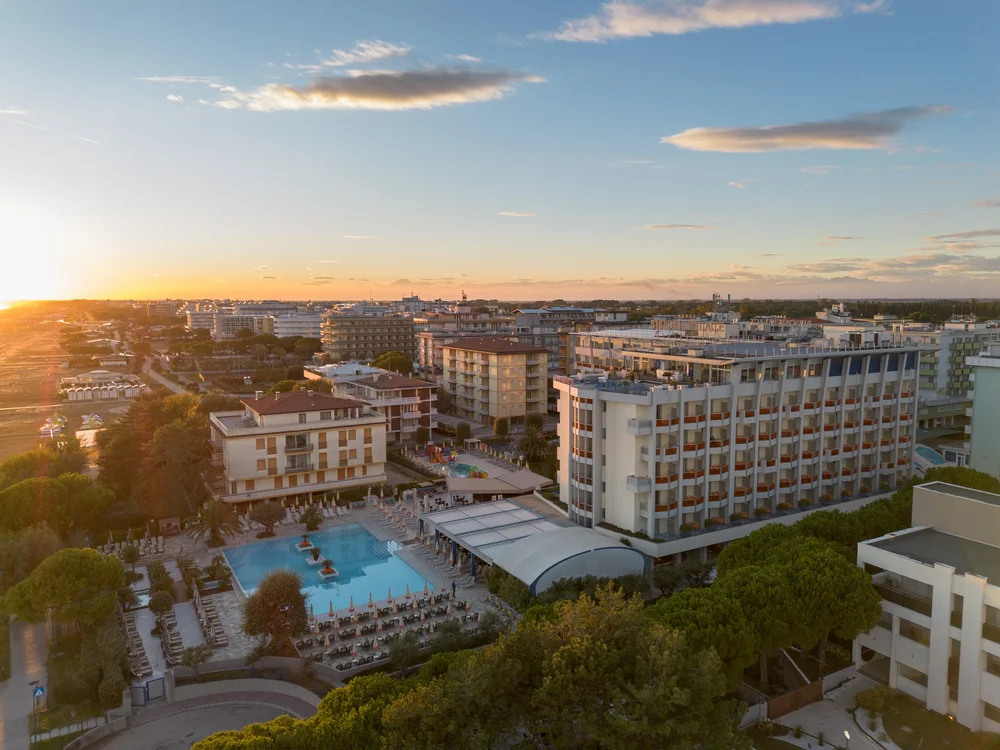 Bibione Palace Hotel · La tua casa al mare a 4 stelle S Vista aerea di un hotel con piscina al tramonto in una località turistica