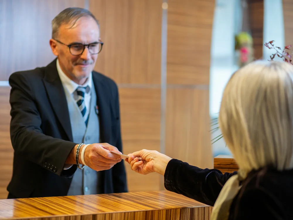 Bibione Palace Hotel · La tua casa al mare a 4 stelle S Receptionist che riceve la carta da una cliente alla reception di un hotel