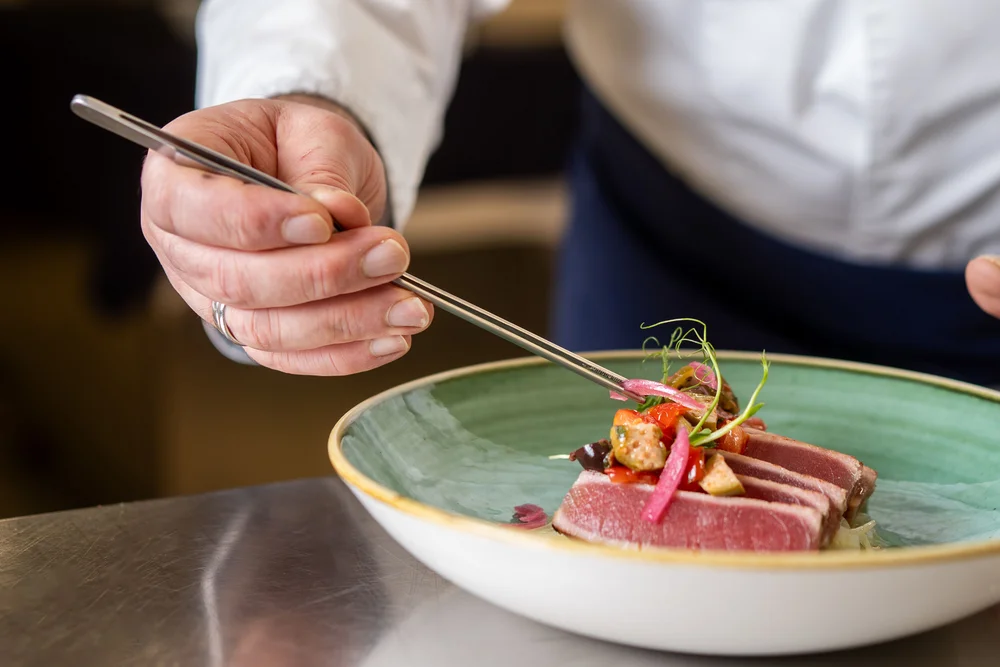 Chef che sistema con pinzette un piatto di tonno e verdure