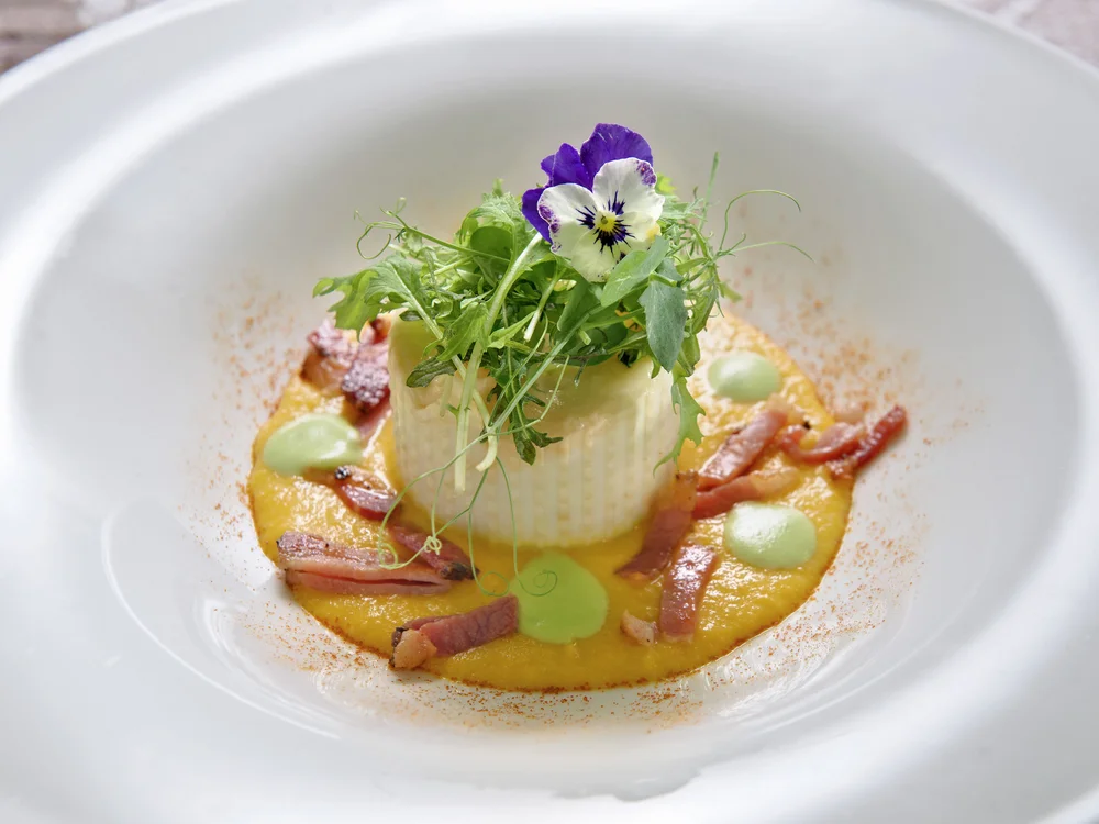Bibione Palace Hotel · La tua casa al mare a 4 stelle S piatto gourmet con crema arancione, strisce di pancetta, crema verde e fiore commestibile