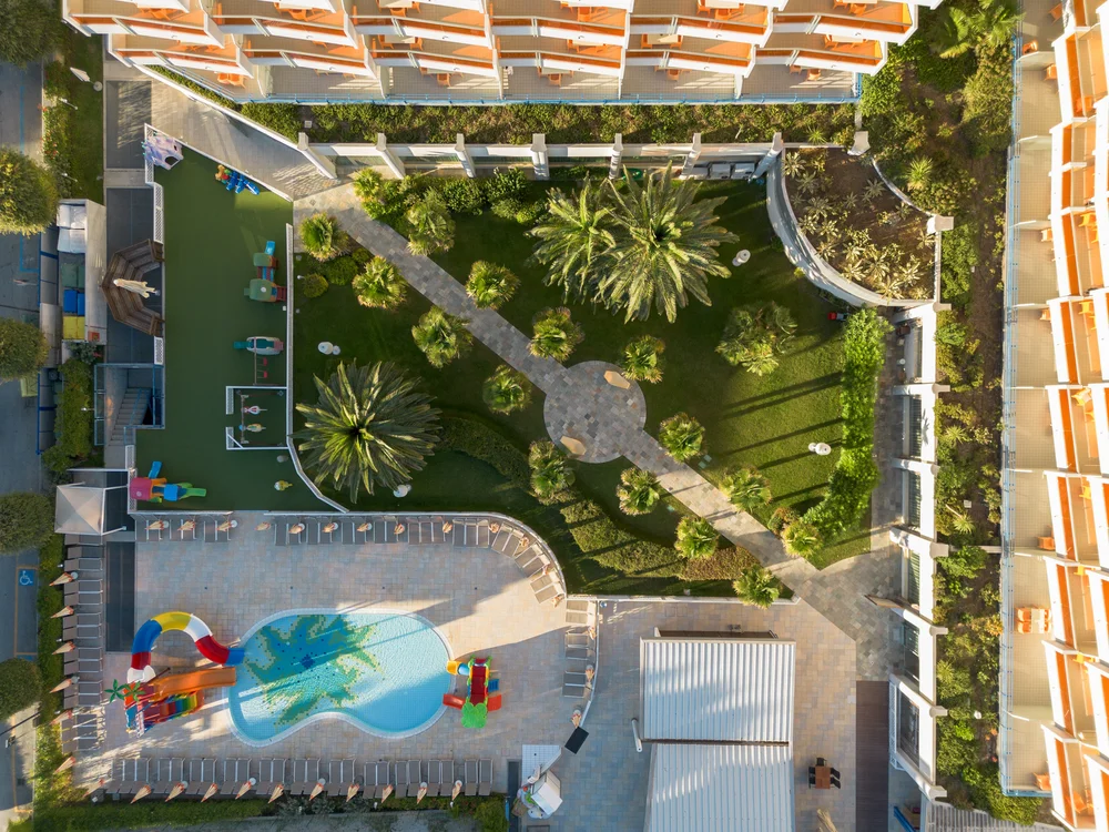 Bibione Palace Hotel · La tua casa al mare a 4 stelle S Vista aerea di un giardino con piscina e scivolo colorato in un hotel