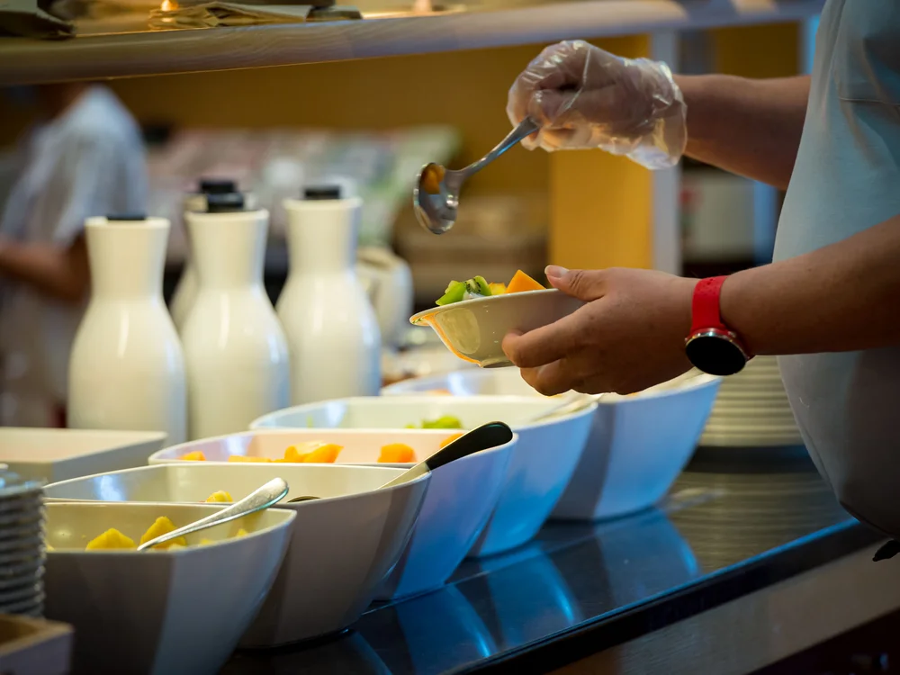 Bibione Palace Hotel · La tua casa al mare a 4 stelle S Persona che serve frutta fresca da un buffet in ciotole bianche