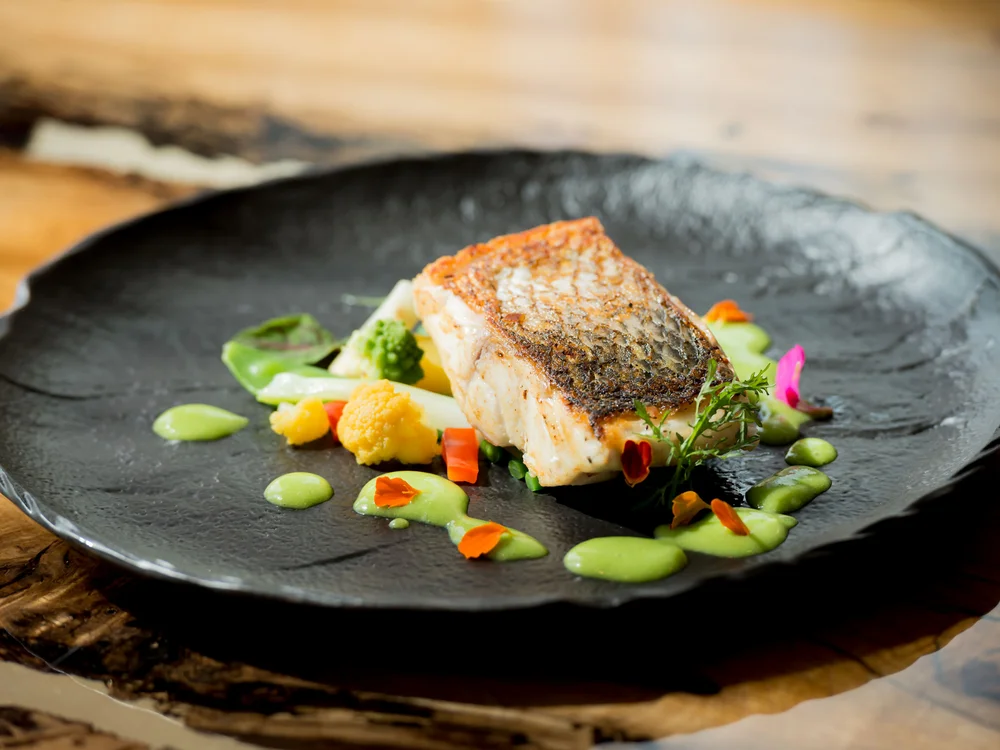 Bibione Palace Hotel · La tua casa al mare a 4 stelle S Filetto di pesce con verdure e salsa verde su piatto nero