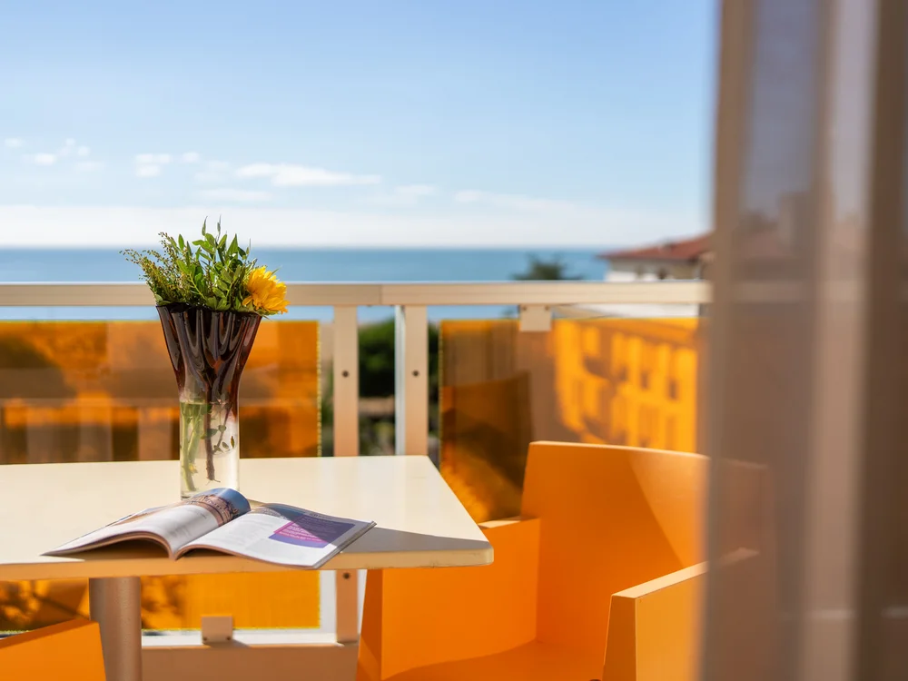 Bibione Palace Hotel · La tua casa al mare a 4 stelle S Balcone con tavolo, vaso di fiori e vista sul mare in giornata soleggiata