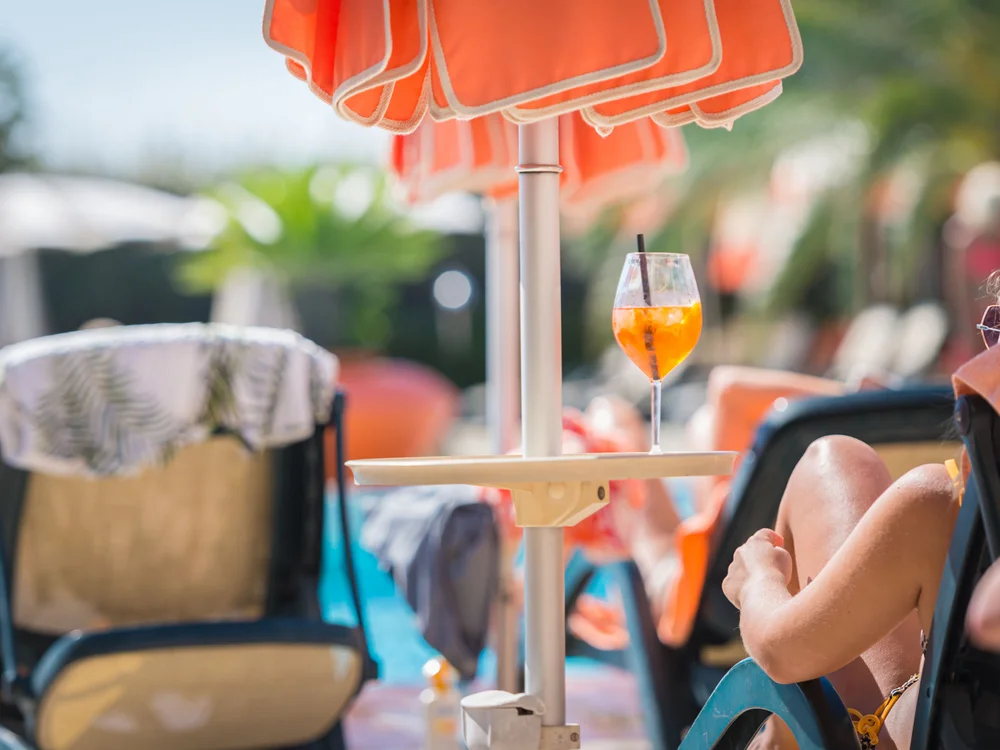 Bibione Palace Hotel · La tua casa al mare a 4 stelle S Ombrellone arancione con bicchiere di cocktail vicino a piscina e persone