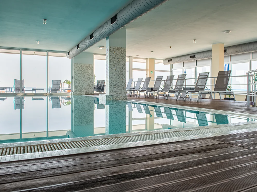 Bibione Palace Hotel · La tua casa al mare a 4 stelle S Piscina interna con sedie a sdraio e grandi finestre