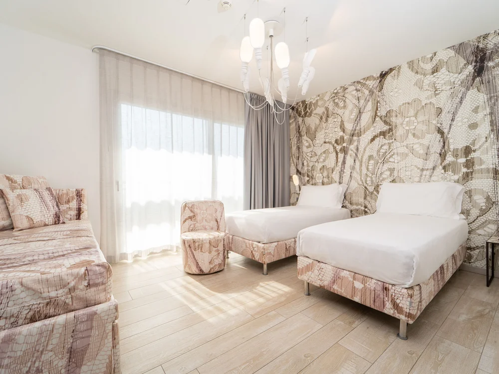 Bibione Palace Hotel · La tua casa al mare a 4 stelle S Camera d'hotel con due letti singoli, divano e parete decorata con motivi floreali