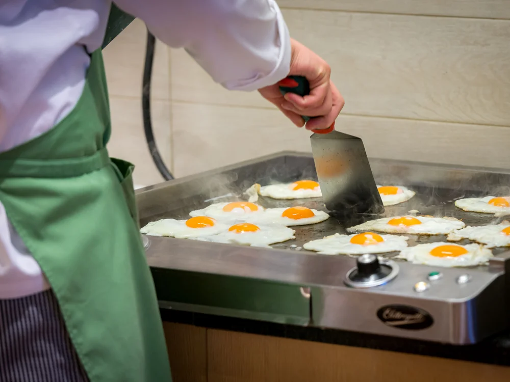 Bibione Palace Hotel · La tua casa al mare a 4 stelle S Cuoco che cucina uova fritte su una piastra in cucina