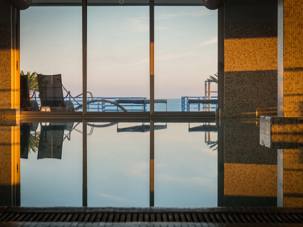 Bibione Palace Hotel · La tua casa al mare a 4 stelle S Piscina interna con vista sul mare al tramonto e sedie a sdraio all'esterno
